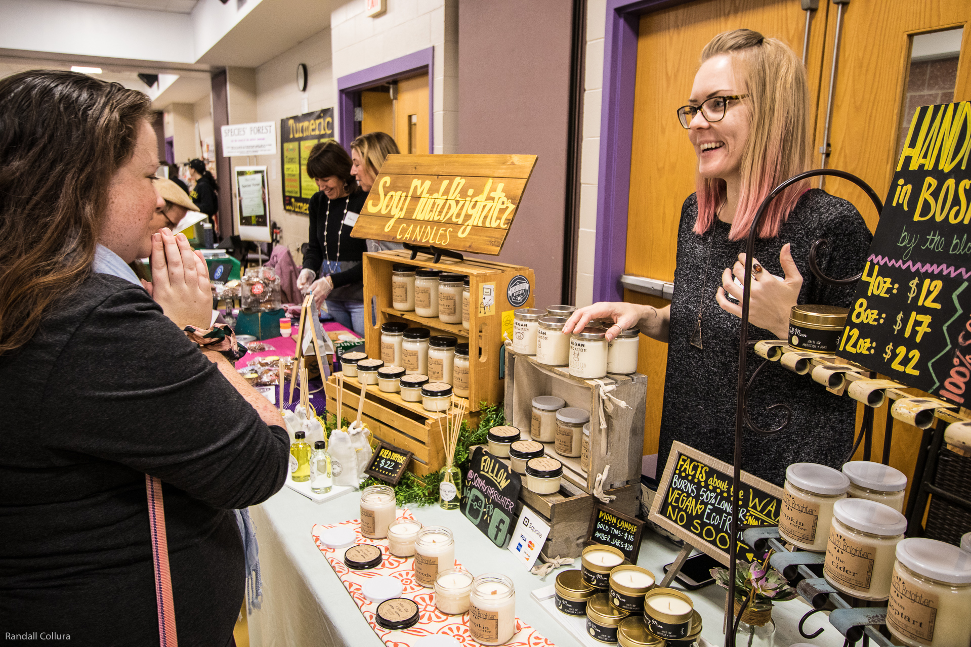 Two women talk, smiling, about a display of soy candles