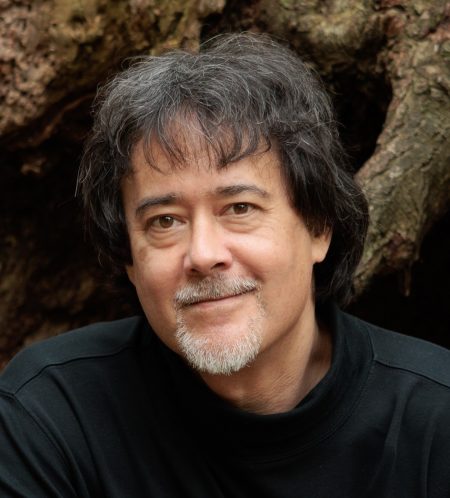 John Sanbonmatsu sitting at the roots of a large tree