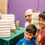 Michael Greger holds up his book, How Not to Die, while posing for a photo with two young fans